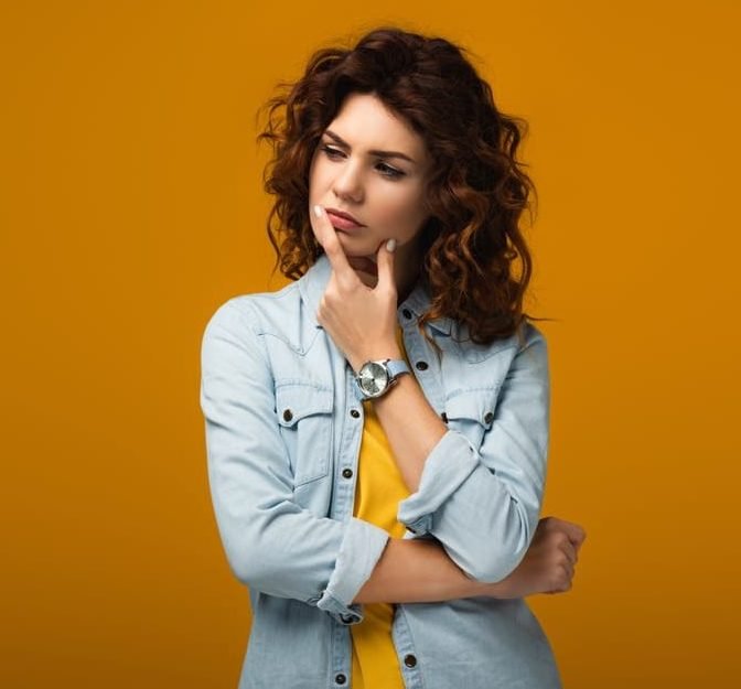 Pensive curly redhead woman thinking to herself