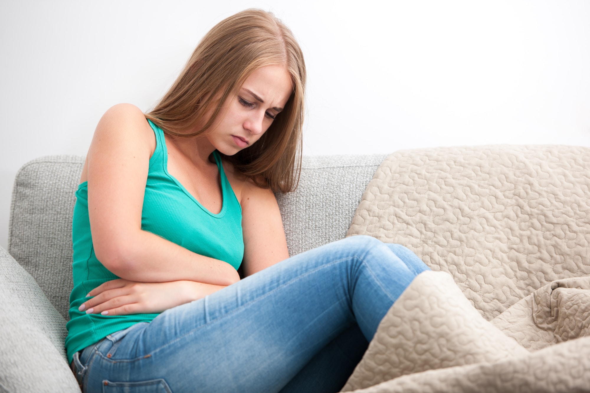 Girl on couch holding her stomach in pain