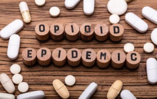 wood sign spelling out opioid epidemic with spilled drugs on surface