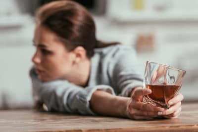 Sad woman holding whiskey glass at table