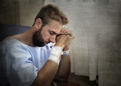 young man in hospital room sitting alone in pain worried for his health condition